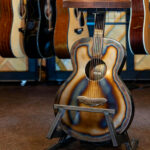 Banquinho de metal na forma de violão com assento de madeira